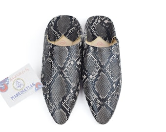 May include: A pair of black and gray snake-skin patterned slippers. The slippers have a pointed toe and a closed back.