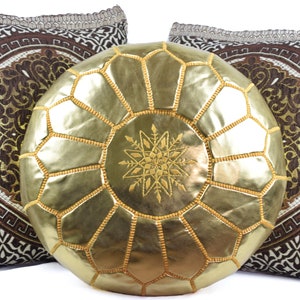 May include: A gold leather pouf with a star design in the center, surrounded by two brown and white patterned throw pillows.