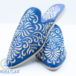May include: A pair of blue leather slippers with silver embroidery. The slippers have a pointed toe and a closed back. The embroidery features a floral design.