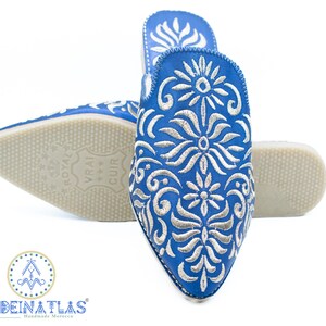 May include: A pair of blue leather slippers with silver embroidery. The slippers have a pointed toe and a flat sole. The embroidery features a floral design.