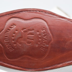 May include: Close-up of the brown leather sole of a white shoe with the text "BEN DAHMEN" and "ROYALE" embossed in a shield shape.