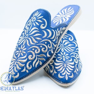 May include: A pair of blue leather slippers with silver embroidery. The slippers have a pointed toe and a closed back. The embroidery features a floral design.