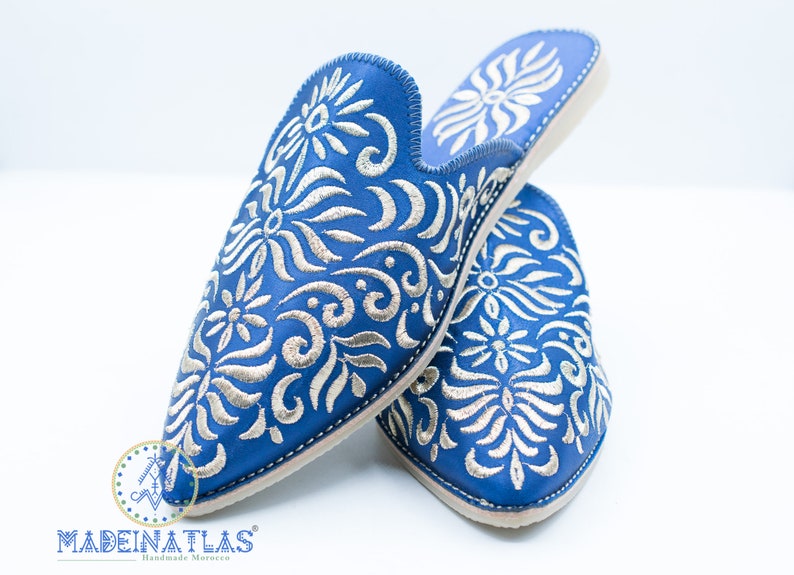 May include: A pair of blue leather slippers with silver embroidery. The slippers have a pointed toe and a closed back. The embroidery features a floral design.