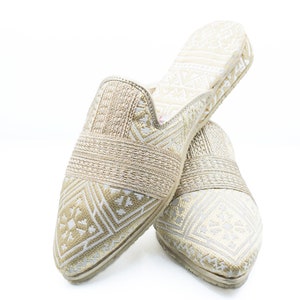 May include: A pair of gold and white patterned slippers with a pointed toe.
