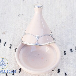 May include: A light pink ceramic tagine with a silver lid and decorative trim. The tagine is open and the lid is resting on top of the base.