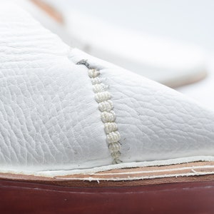 May include: Close-up of a white leather shoe with a red sole and a white stitching detail.