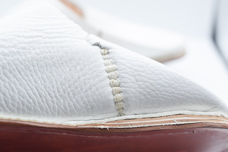 May include: Close-up of a white leather shoe with a red sole and a white stitching detail.