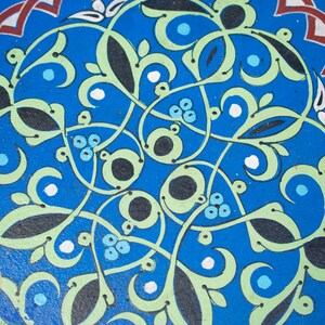May include: A blue circular design with intricate green, black, and white floral patterns. The design is reminiscent of traditional Moroccan tilework.