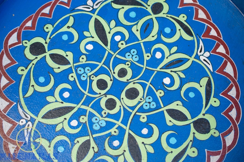 May include: A blue circular design with intricate green, black, and white floral patterns. The design is reminiscent of traditional Moroccan tilework.