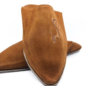 Peut inclure: Une paire de pantoufles en daim marron &agrave; bout pointu. Les pantoufles ont un design simple et sont brod&eacute;es d'une petite lettre "R" stylis&eacute;e sur le dessus.