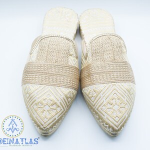 May include: A pair of gold embroidered slippers with pointed toes. The slippers have a geometric pattern and a gold band across the top.