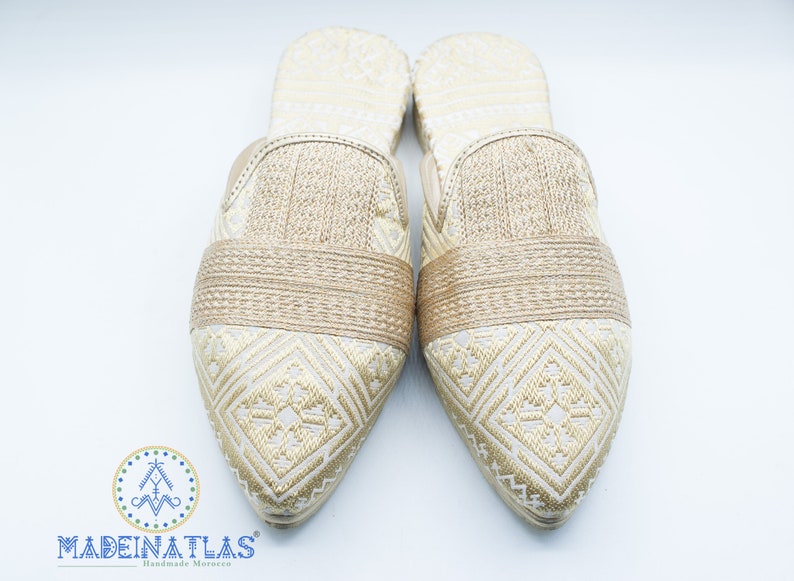 May include: A pair of gold embroidered slippers with pointed toes. The slippers have a geometric pattern and a gold band across the top.