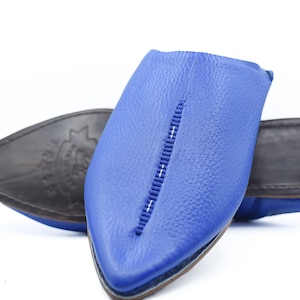 Puede incluir: Un par de zapatillas de cuero azul con punta puntiaguda y un detalle de costura blanca. Las zapatillas están hechas de cuero suave y tienen un ajuste cómodo.