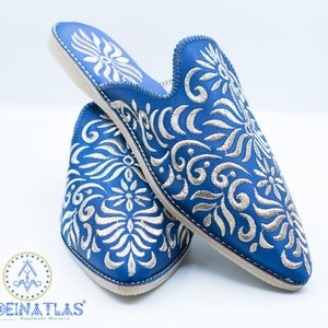May include: A pair of blue leather slippers with silver embroidery. The slippers have a pointed toe and a flat sole. The embroidery features a floral design.