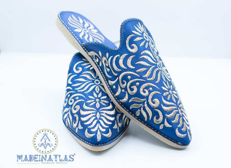 May include: A pair of blue leather slippers with silver embroidery. The slippers have a pointed toe and a flat sole. The embroidery features a floral design.