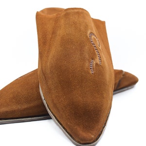Peut inclure: Une paire de pantoufles en daim marron &agrave; bout pointu. Les pantoufles ont un design simple et sont brod&eacute;es d'une petite lettre "R" stylis&eacute;e sur le dessus.