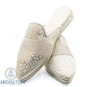 May include: A pair of gold and white patterned slippers with a pointed toe. The slippers are made of a soft, woven fabric and have a comfortable fit.