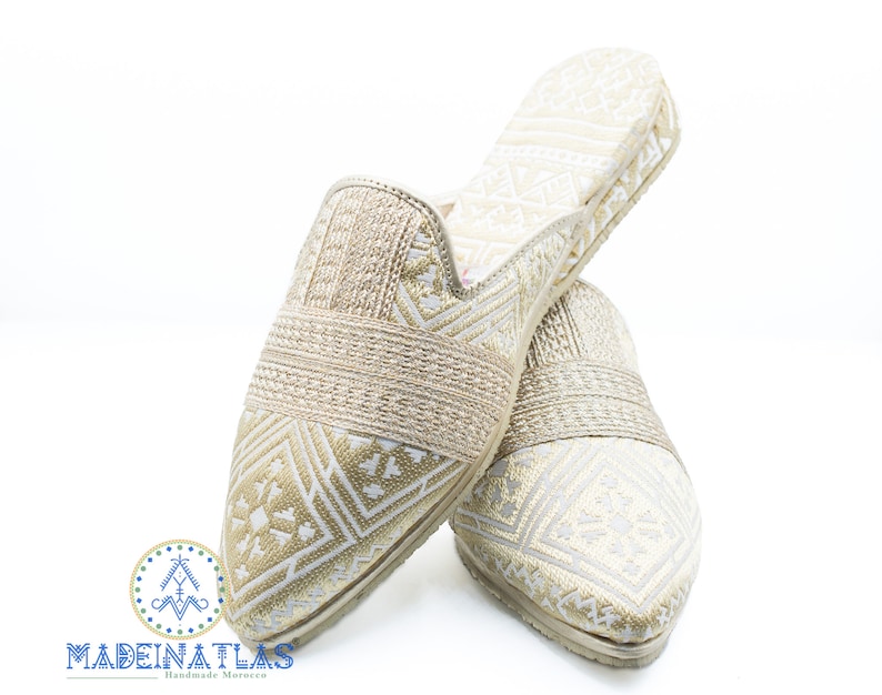 May include: A pair of gold and white patterned slippers with a pointed toe. The slippers are made of a soft, woven fabric and have a comfortable fit.