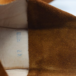 Peut inclure: Gros plan de l'int&eacute;rieur d'une chaussure en daim marron avec une &eacute;tiquette bleue indiquant "42" et "37".