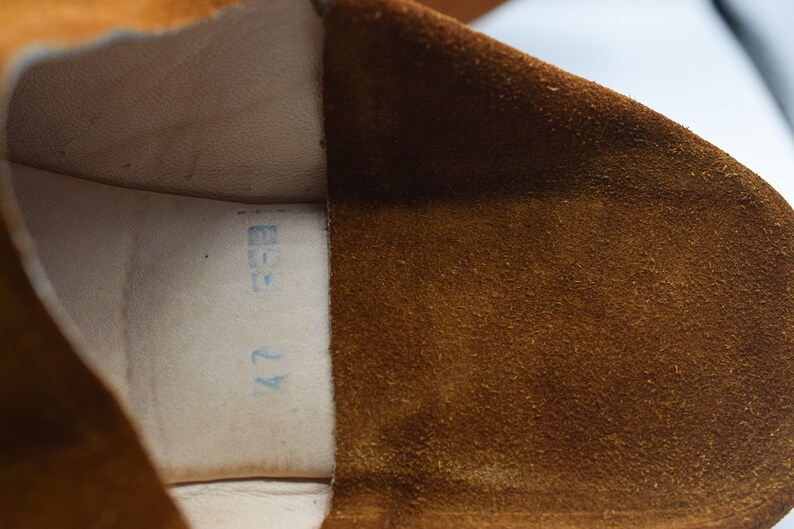 Peut inclure: Gros plan de l'int&eacute;rieur d'une chaussure en daim marron avec une &eacute;tiquette bleue indiquant "42" et "37".