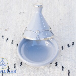 May include: A light blue ceramic dish with a lid. The lid has a silver trim and a decorative design. The dish is open and the lid is resting on top of it.