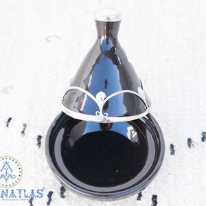 May include: A black tagine with a silver lid and decorative trim. The tagine is a traditional Moroccan cooking pot.