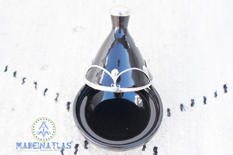 May include: A black tagine with a silver lid and decorative trim. The tagine is a traditional Moroccan cooking pot.