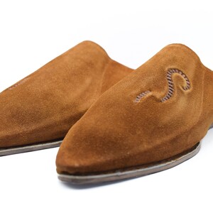 Peut inclure: Une paire de pantoufles en daim marron avec une pointe pointue et un simple motif brod&eacute;.