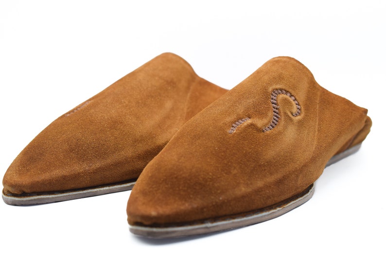 Peut inclure: Une paire de pantoufles en daim marron avec une pointe pointue et un simple motif brod&eacute;.