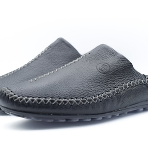 Puede incluir: Un par de zapatos negros de cuero sin cordones con un detalle de costura decorativa alrededor del borde de la suela.