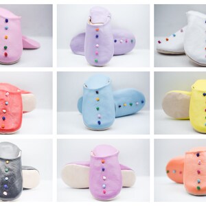 Op de afbeelding: Een verzameling kleurrijke leren slippers in verschillende tinten, waaronder roze, paars, wit, rood, blauw, geel, grijs en oranje. Elke slipper heeft een rij kleine, veelkleurige decoratieve kralen in het midden.