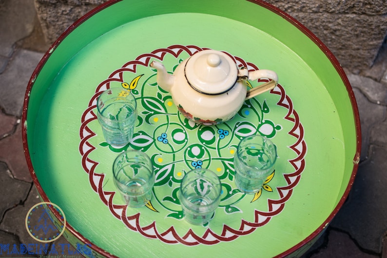 May include: A green tray with a white teapot and five clear glasses. The tray has a decorative design with red, white, and green colors.
