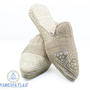 May include: A pair of gold and white patterned slippers with a pointed toe. The slippers have a woven strap across the top and a geometric pattern.