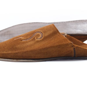 Peut inclure: Une paire de pantoufles en daim marron avec un motif brod&eacute; d&eacute;coratif. Les pantoufles ont une pointe pointue et une semelle plate.