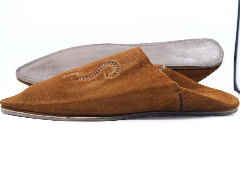 Peut inclure: Une paire de pantoufles en daim marron avec un motif brod&eacute; d&eacute;coratif. Les pantoufles ont une pointe pointue et une semelle plate.