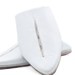 May include: A pair of white leather slippers with pointed toes and a decorative stitch down the center of each shoe.