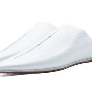May include: A pair of white leather slippers with a pointed toe and a stitched seam down the center of the shoe.