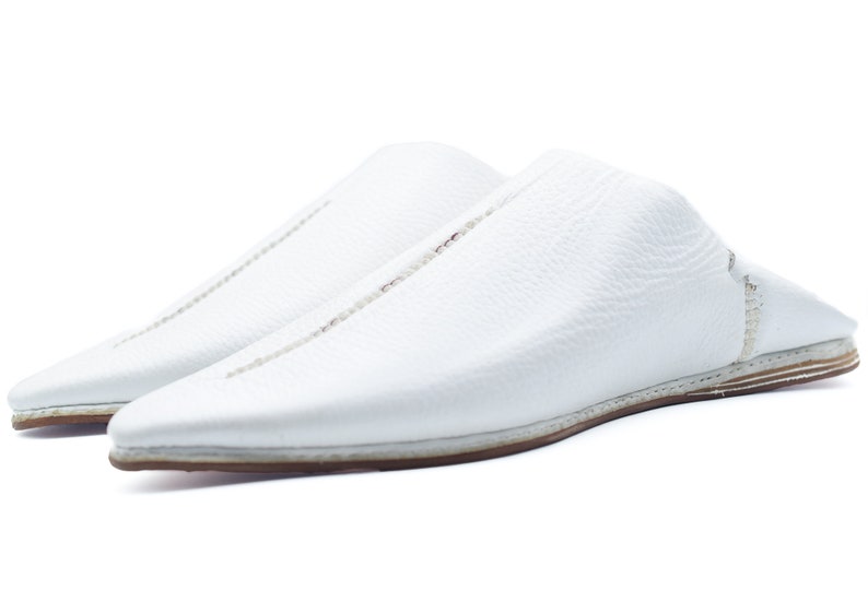 May include: A pair of white leather slippers with a pointed toe and a stitched seam down the center of the shoe.