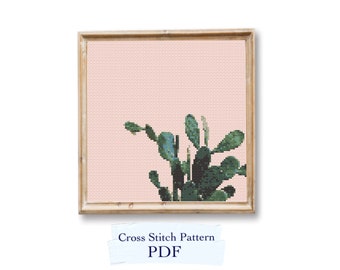 May include: A cross stitch pattern featuring a cactus plant in shades of green against a light pink background. The pattern is framed in a light wood frame. The text "Cross Stitch Pattern PDF" is visible below the frame.