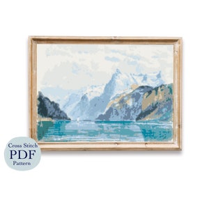 May include: A cross stitch pattern PDF for a scenic landscape with snow-capped mountains, a lake, and a small boat in the distance. The mountains are a light blue and gray, and the lake is a vibrant blue. The sky is a light blue with white clouds.