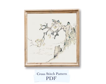 May include: A framed cross stitch pattern depicting a delicate, stylised tree with white blossoms and a rocky cliff in the background. The pattern is in shades of grey, white, and light brown. The frame is a simple, light wood.