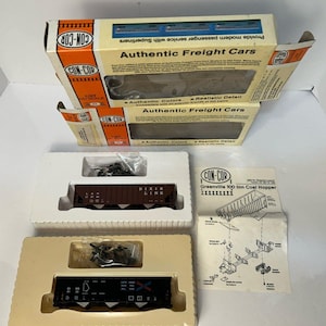 May include: Several model train freight cars, including a brown "Dixie Line" car and a black car with white markings, are displayed in their original packaging. The boxes are labeled "Authentic Freight Cars" and "CON-COR".