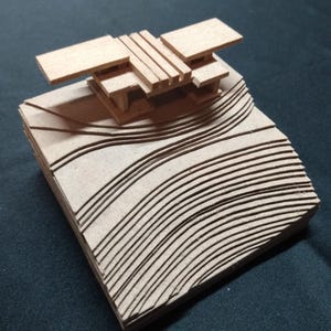 May include: A light brown architectural model made of stacked cardboard layers. The base features curved, grooved lines representing topography, while the top section consists of flat, rectangular platforms supported by vertical pillars.