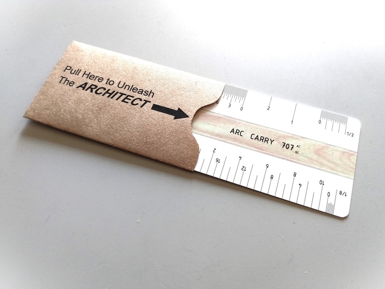 Pu&ograve; includere: Un righello bianco con segni neri etichettati "ARC CARRY 707" e una striscia di legno con una trama a venature del legno. Il righello &egrave; in una busta di carta marrone con il testo "Pull Here to Unleash The ARCHITECT" stampato su di essa.