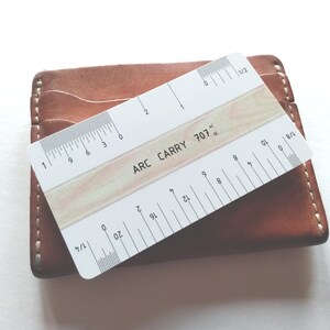 Pu&ograve; includere: Un righello di plastica bianco con segni neri, etichettato "ARC CARRY 707". Il righello &egrave; lungo 15,24 cm e ha segni per 1/2, 1/4, 1/8 e 1/16 di pollice.