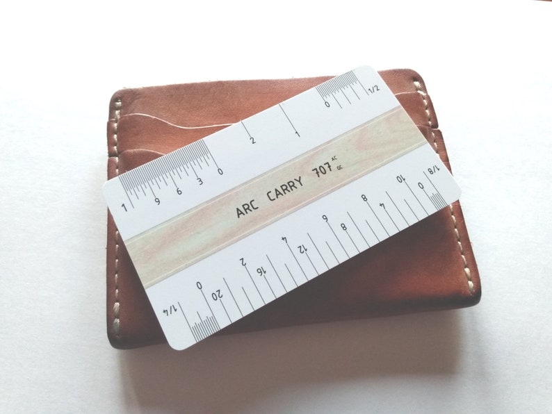 Pu&ograve; includere: Un righello di plastica bianco con segni neri, etichettato "ARC CARRY 707". Il righello &egrave; lungo 15,24 cm e ha segni per 1/2, 1/4, 1/8 e 1/16 di pollice.
