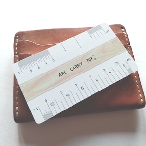 May include: A white plastic ruler with black markings, labelled "ARC CARRY 707". The ruler is 15.24 cm long and has markings for 1/2, 1/4, 1/8, and 1/16 inches.