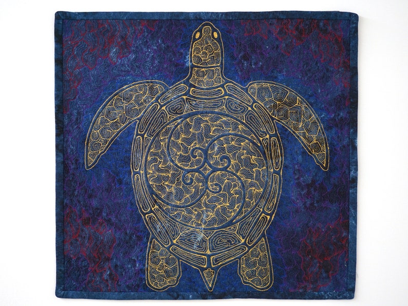 Może przedstawiać: Wz&oacute;r haftowany złotą nicią przedstawiający morską ż&oacute;łwia na niebieskim tle z tkaniny. Ż&oacute;łw jest bogato zdobiony wirującym wzorem wewnątrz swojego pancerza.