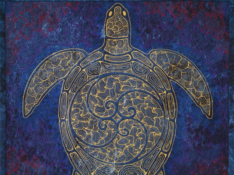 Może przedstawiać: Wz&oacute;r haftowany złotą nicią przedstawiający morską ż&oacute;łwia na tle niebieskiego i fioletowego materiału. Ż&oacute;łw jest obwiedziony złotą nicią i ma szczeg&oacute;łowy wz&oacute;r pancerza.