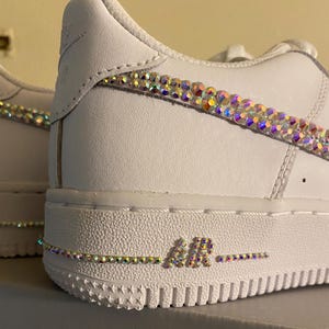 May include: White leather sneakers with iridescent rhinestones on the swoosh and around the "AIR" logo on the sole.